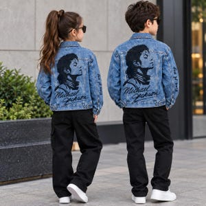 Op de afbeelding: Twee personen dragen bijpassende blauwe spijkerjacks met een zwarte grafische print van Michael Jackson op de achterkant, vergezeld van de tekst "Michael Jackson" en "King of pop" op de mouwen, gecombineerd met zwarte broeken en witte sneakers.