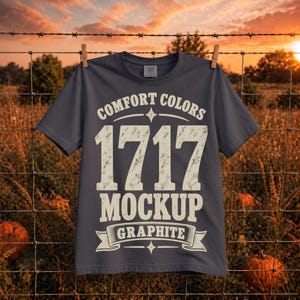 May include: A graphite grey short-sleeve t-shirt featuring distressed white text that reads COMFORT COLORS 1717 MOCKUP GRAPHITE. The shirt has a crew neckline and a standard fit, with the graphic centred on the front of the garment.