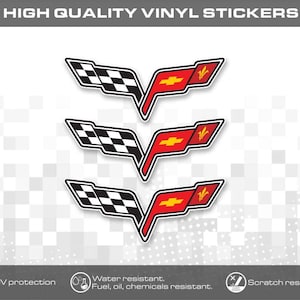 May include: Three vinyl stickers featuring the Chevrolet Corvette emblem, which consists of a black and white checkered flag on the left and a red section on the right containing a yellow Chevrolet bowtie logo and a yellow fleur-de-lis symbol.