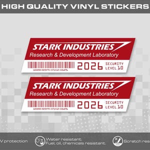Könnte beinhalten: Zwei rechteckige Vinylaufkleber in Rot und Weiß mit dem Text STARK INDUSTRIES Research & Development Laboratory, einem Strichcode, der Jahreszahl 2026 und Security Level 10. Die Aufkleber sind UV-geschützt sowie wasser- und kratzfest.