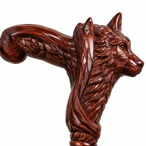 May include: A polished dark brown wooden cane handle featuring a detailed, hand-carved wolf head. The sculpture displays intricate fur textures, pointed ears, and a smooth, glossy finish that extends into the curved grip of the walking stick.