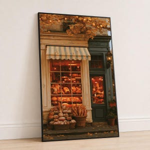 Puede incluir: Una impresión de arte mural vertical enmarcada que representa la fachada de una panadería con un toldo a rayas, grandes ventanales llenos de varios panes y cestas de pan en la acera, todo iluminado por una cálida luz interior dorada.