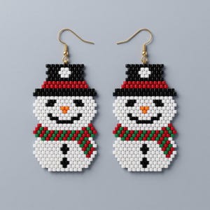 May include: A pair of beaded dangle earrings shaped like snowmen. Each snowman features a black top hat with a white band, a white head with a black face and orange nose, and a white body with a red and green striped scarf and black buttons.