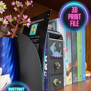May include: A black 3D printed bookshelf with two drawers and a moon and star design on the front. The bookshelf is on a wooden shelf with several books behind it. The text "3D Print File" is in a neon pink circle above the bookshelf.