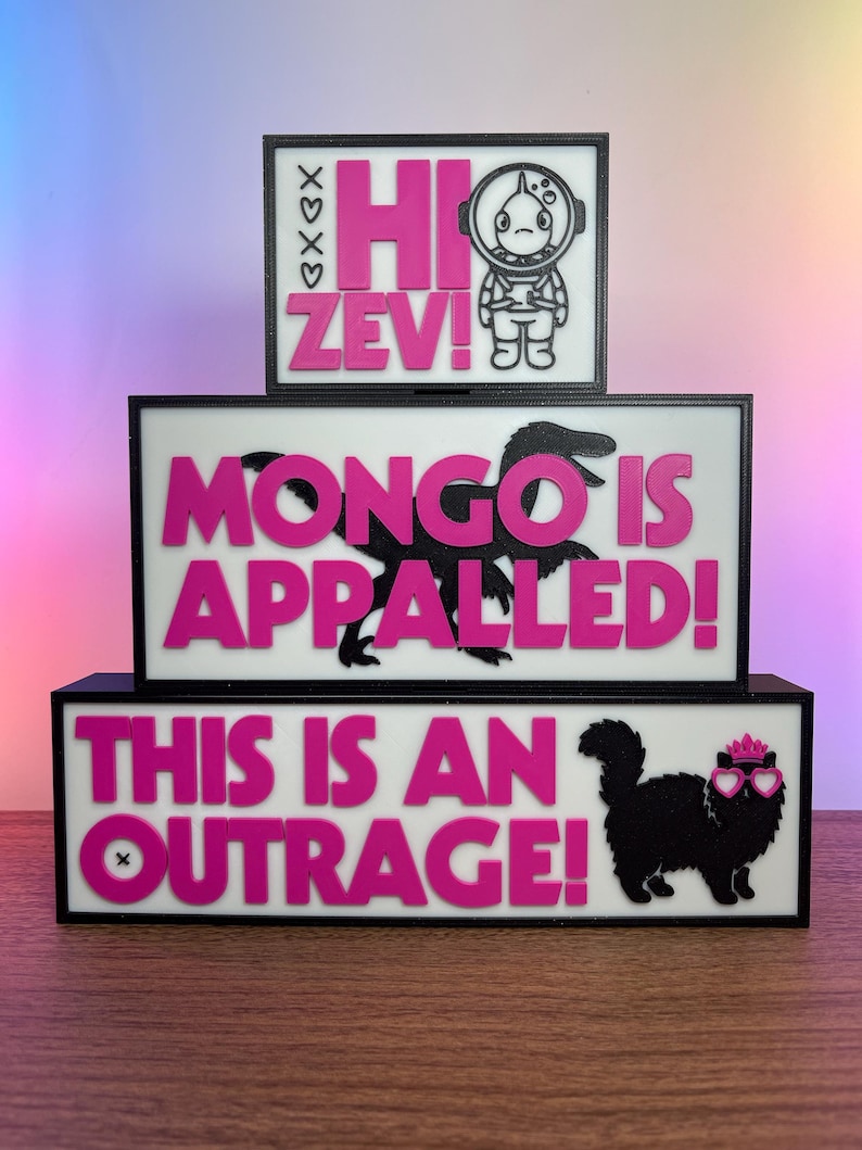 Puede incluir: Carteles de tres niveles, con marco negro, fondos blancos y texto rosa. El letrero superior dice "Hi Zev!" con un astronauta de dibujos animados. El letrero del medio dice "Mongo is Appalled!" con una silueta de dinosaurio. El letrero inferior dice "This is an Outrage!" con un gato.
