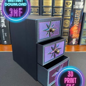 Puede incluir: Un organizador negro de tres cajones con un diseño en forma de estrella en cada cajón. Los cajones son de color púrpura y azul iridiscente con una perilla dorada. El organizador está sentado sobre una superficie de madera. INSTANT DOWNLOAD 3MF 3D PRINT FILE