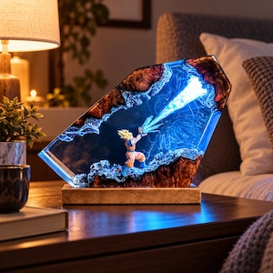 Puede incluir: Una lámpara personalizada de resina y madera con una figura en miniatura de pelo puntiagudo con un traje naranja y azul, situada entre dos bordes de madera oscura, emitiendo un efecto de haz de luz azul brillante.