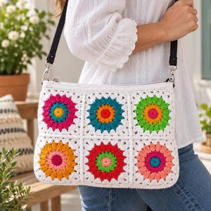 Peut inclure: Un sac à bandoulière en crochet rectangulaire composé de six carrés à bordure blanche, chacun présentant un motif floral multicolore vif dans des tons de rose, jaune, bleu sarcelle, orange, rouge et vert. Le sac possède une sangle noire.