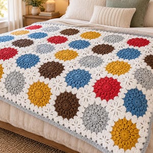 Peut inclure: Une couverture au crochet présentant un motif répétitif de cercles rouges, bleus, jaunes, marron et gris clair, reliés par des connecteurs blancs en forme de fleurs. La couverture possède une bordure gris clair et recouvre un lit aux tons neutres.