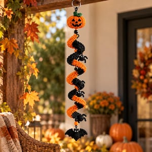 May include: A hanging spiral decoration featuring a crocheted orange jack-o'-lantern at the top and a black bat at the bottom. The spiral is made of alternating orange and black yarn segments, accented with small black spiders and beads.