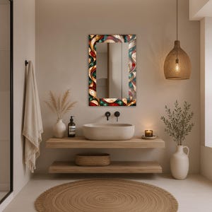 Op de afbeelding: Een rechthoekige wandspiegel met een decoratieve lijst voorzien van een levendig, meerkleurig glas-in-loodpatroon in dieprode, groenblauwe en gouden tinten, gekenmerkt door ingewikkelde, wervelende organische vormen en een glanzend, reflecterend oppervlak.