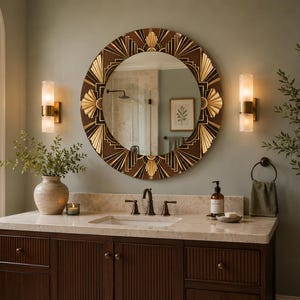 May include: A round wall mirror featuring a dark brown and gold frame with a geometric sunburst pattern. The mirror has a reflective glass center and is mounted on a wall above a bathroom vanity with a stone countertop and sink.