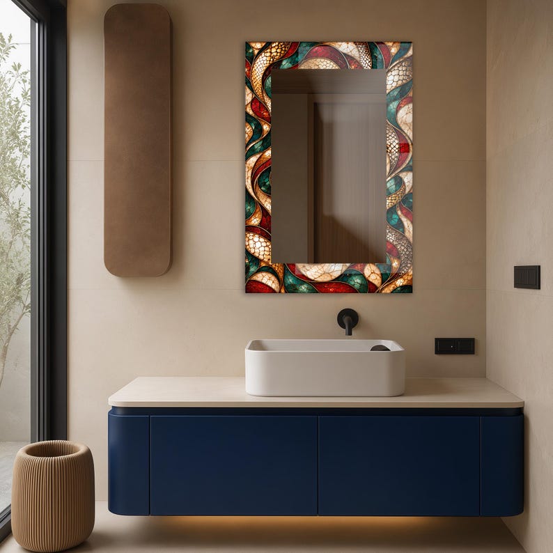 Op de afbeelding: Een rechthoekige wandspiegel met een decoratieve lijst met een glas-in-loodpatroon in tinten dieprood, smaragdgroen en cr&egrave;me. De spiegel is gemonteerd boven een witte rechthoekige waskom en een donkerblauw zwevend wastafelmeubel.