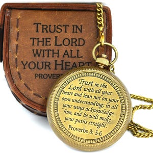 Puede incluir: Un reloj de bolsillo de color latón con cadena, que presenta el texto grabado "Trust in the Lord with all your heart and lean not on your own understanding; in all your ways acknowledge him, and he will make your paths straight. Proverbs 3: 5-6".
