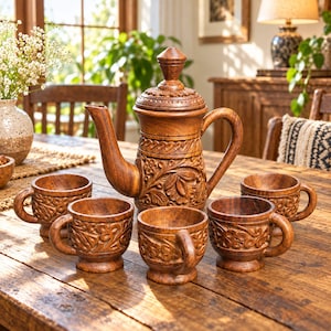 Peut inclure: Un service à thé en bois marron composé d'une théière avec couvercle et de quatre tasses assorties. Chaque pièce présente des motifs floraux et végétaux sculptés à la main sur les surfaces extérieures, avec une finition polie et un grain naturel.