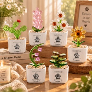 May include: Six glass plant ornaments in white square pots, each featuring a paw print graphic and the text "No longer by my side, forever in my heart, in loving memory of Charlie." The plants include a cactus, pink flowers, daisies, and succulents.
