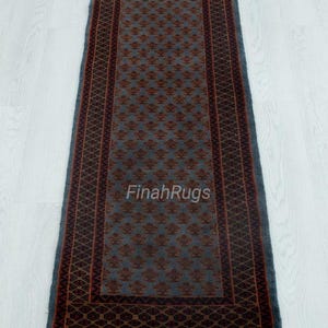 May include: A rectangular runner rug featuring a slate blue field with a repeating pattern of small dark red floral motifs. The rug is framed by a dark red border with a geometric diamond design and finished with light tan fringe at both ends.