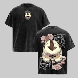 May include: A black acid-wash t-shirt featuring a small graphic on the front with the text YIP YIP and a creature icon. The back displays a large, detailed illustration of a furry creature with horns, surrounded by pink cloud motifs.
