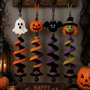 May include: Four hanging crochet Halloween decorations featuring a white ghost, an orange pumpkin, a black bat, and a green-faced witch. Each figure sits atop a spiralling yarn tail in alternating colours, ending in a black witch hat with a buckle.
