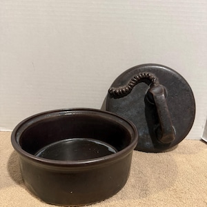 May include: A dark brown ceramic lidded bowl with a smooth finish. The circular lid features a sculptural handle shaped like a vintage telephone handset, complete with a coiled cord detail molded directly onto the top surface of the lid.