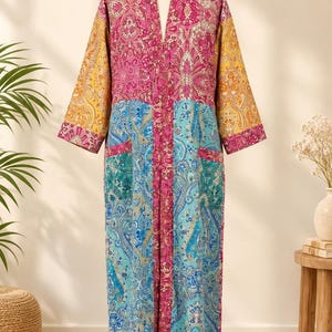 May include: A long-sleeved robe featuring a patchwork design with various paisley and floral patterns in vibrant shades of pink, blue, yellow, and teal. The garment has an open front, a V-neckline, and two front pockets, displayed on a mannequin.