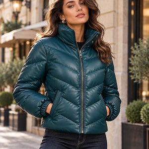 Könnte beinhalten: Eine dunkel-petrolfarbene Steppjacke mit glatter, lederartiger Oberfläche und Chevron-Steppmuster. Die Jacke verfügt über einen hohen Stehkragen, einen durchgehenden Metallreißverschluss, lange Ärmel mit elastischen Bündchen und zwei Seitentaschen.