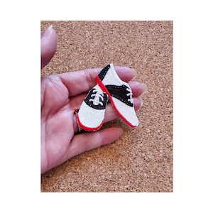 May include: Two black and white saddle shoes with red trim. The shoes are embroidered and are about 2 inches long.