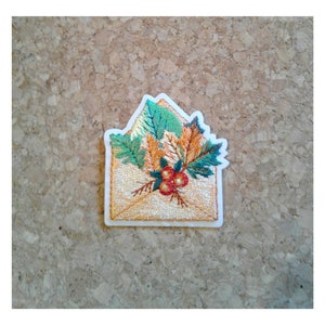 May include: Embroidered iron-on patch featuring a brown envelope with a bouquet of green, orange, and red leaves and berries.
