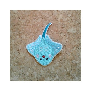 May include: A light blue embroidered patch of a cartoon stingray with a teal tail and a red nose. The stingray has a white outline and a white belly with a pink spot.