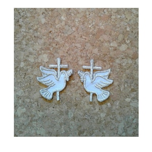 May include: Two white embroidered iron-on patches of a dove with a cross. The dove is white with silver outlining. The cross is silver.