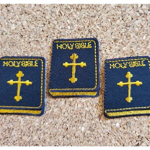 May include: Three black fabric patches with gold stitching. Each patch features a gold cross and the text "HOLY BIBLE".