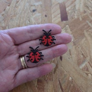 May include: Two small ladybug patches featuring detailed embroidery. Each patch has a vibrant red body with black spots, a black head, and black antennae. The ladybugs are circular in shape with distinct stitched edges, showcasing a high-contrast design.
