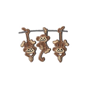 May include: Three brown embroidered monkeys hanging from a gray branch. The monkeys are smiling and have brown eyes.