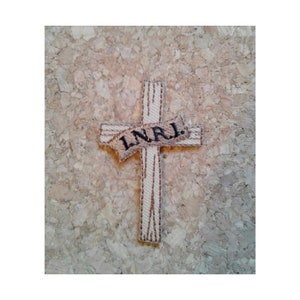 May include: A white cross with brown stitching and a banner that reads "INRI" in black embroidery.