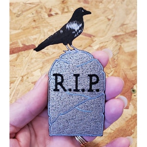 May include: Black crow perched on a gray stone tombstone with the inscription "R.I.P."