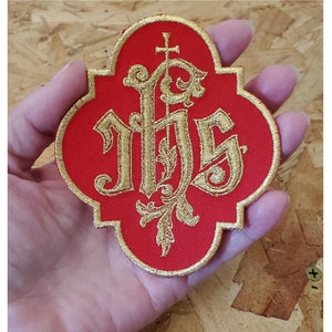 May include: Red felt patch with a gold embroidered monogram of "IHS" with a cross above the letters.
