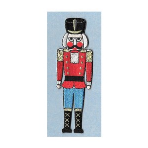 May include: A red and blue embroidered nutcracker with a black hat and white beard. The nutcracker has a gold trim and a black belt.