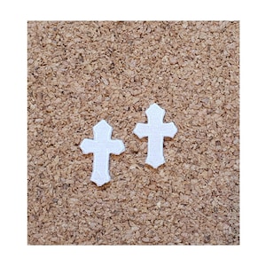 May include: Two white cross shapes on a corkboard background.