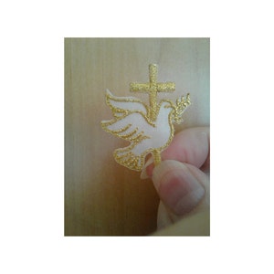 May include: A white dove with gold embroidery, perched on a gold cross, with a branch of olive leaves in its beak.