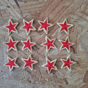 May include: Twelve red embroidered stars with gold outlines on a wood background.