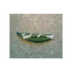 May include: Green embroidered patch of a canoe with two oars. The canoe is green with white stripes and the oars are gold.