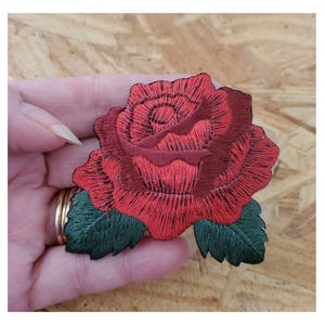 May include: Red embroidered rose patch with green leaves. The rose is detailed with stitching and has a 3D effect.