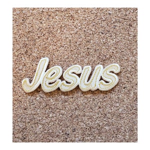 May include: White felt patch with gold embroidery spelling out the word "Jesus" in a cursive font.