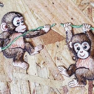 May include: Two brown embroidered monkey patches with green vines. One monkey is holding a vine and the other is hanging from a vine.