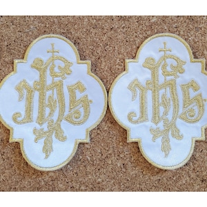 May include: Two white fabric patches with gold embroidery of the letters "IHS" in a stylized font. The letters are surrounded by a decorative floral design.