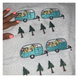 May include: White towel embroidered with four turquoise camper trailers and several green pine trees. The campers have black wheels and are decorated with colorful banners. The towel is soft and fluffy.