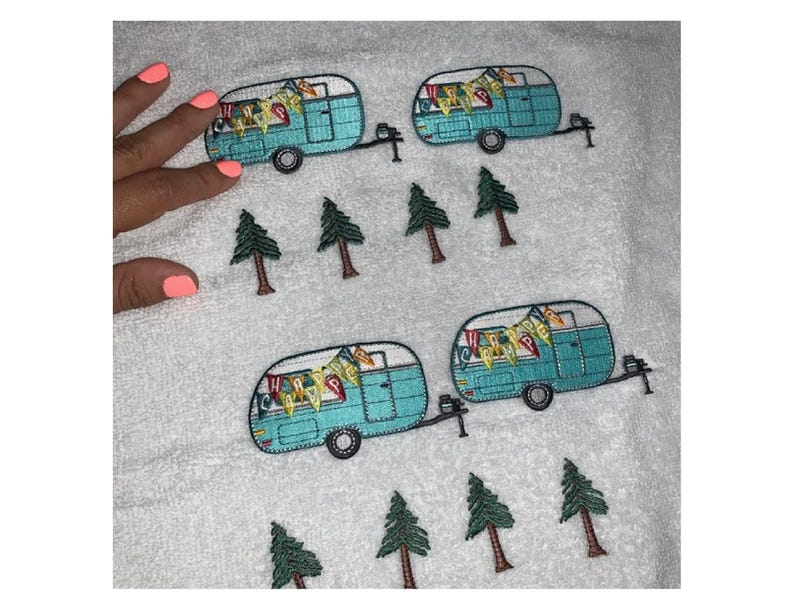 May include: White towel embroidered with four turquoise camper trailers and several green pine trees. The campers have black wheels and are decorated with colorful banners. The towel is soft and fluffy.