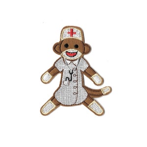 May include: Brown embroidered monkey wearing a white doctor's coat with a red cross on the hat and a stethoscope around its neck.