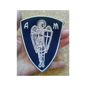 May include: A blue embroidered patch with a white angel holding a shield with a cross. The letters A and M are on either side of the angel.