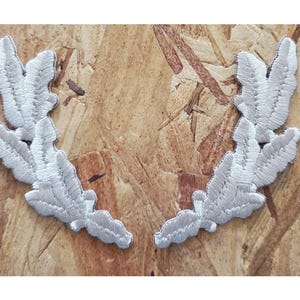 May include: Two silver embroidered fabric patches shaped like a laurel wreath. Each patch has five leaves.